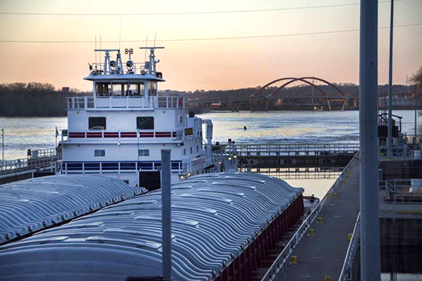 A barge is in a lock and dam unit, with a bridge in the background.